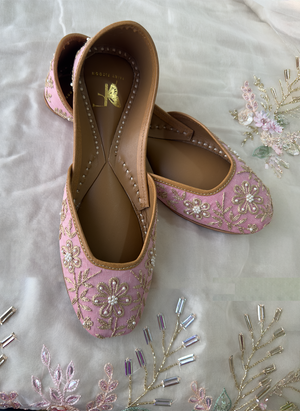 Pair of pink embroidered juttis on a textured fabric background